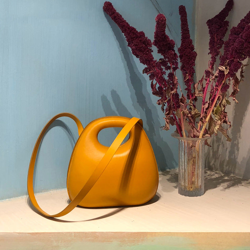 Yellow messenger bag on a light surface with a vase of red flowers
