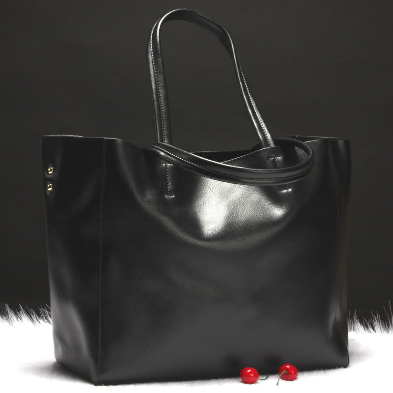 Black leather tote bag on a dark background with red cherries.