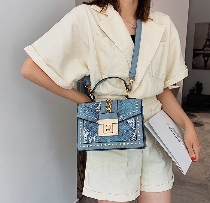 Person holding a blue women's crossbody alligator bag with gold accents