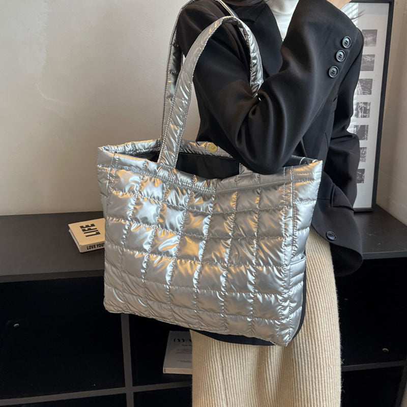 Person holding a silver quilted women's plaid shoulder bag indoors