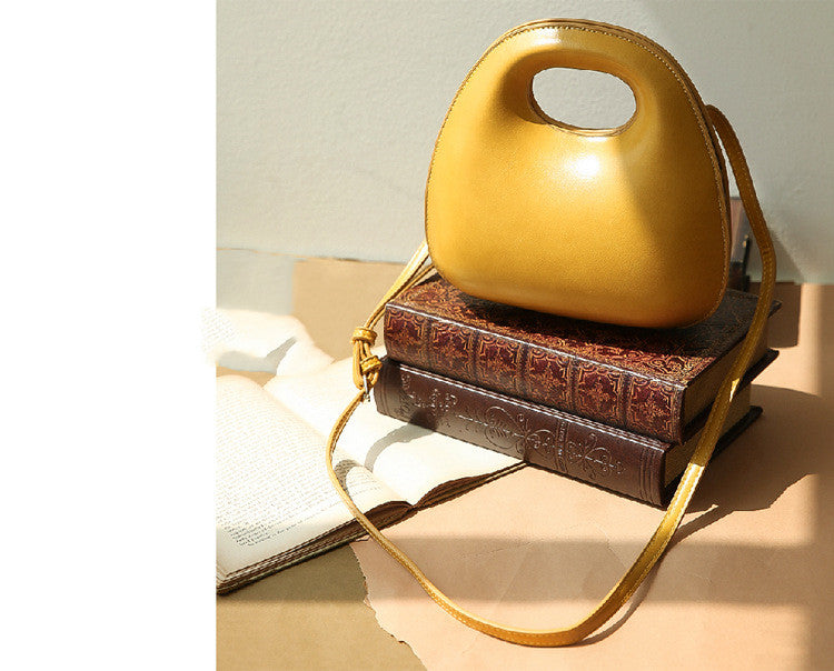 Gold messenger bag with a brown textured base on a light surface