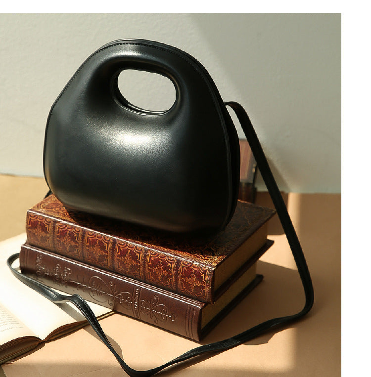 Black messenger bag on a stack of books with a neutral background