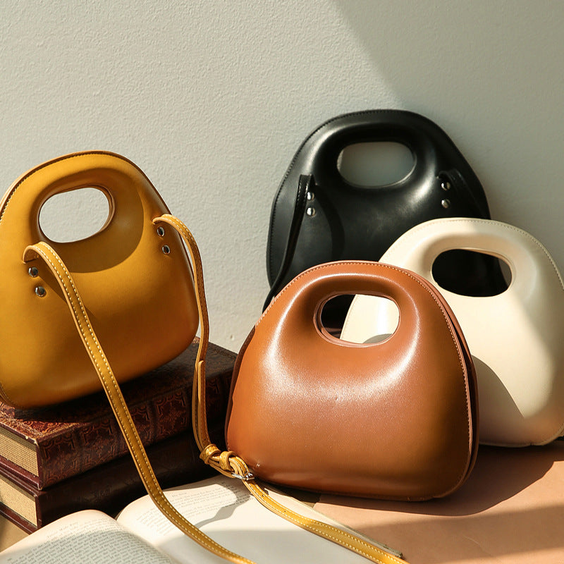 Four messenger bags in yellow, black, brown, and white on a neutral background