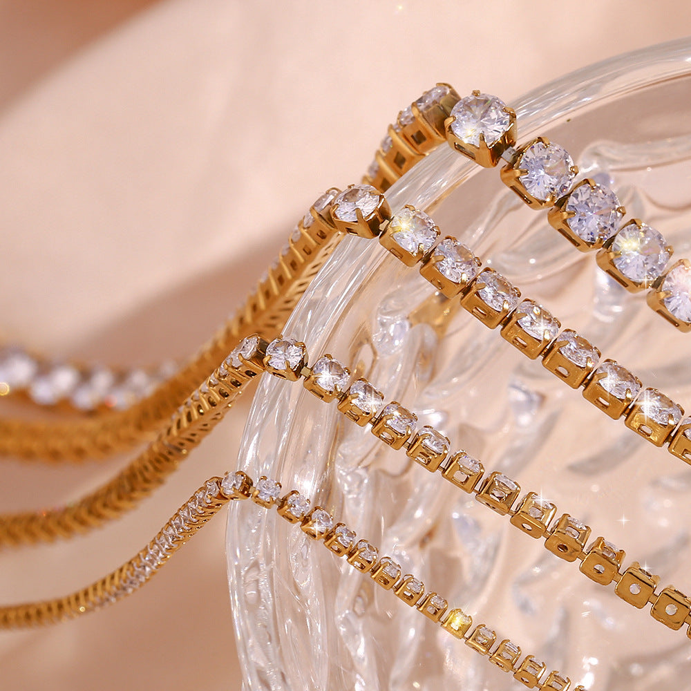 Gold tennis necklace with clear gemstones on a textured beige surface