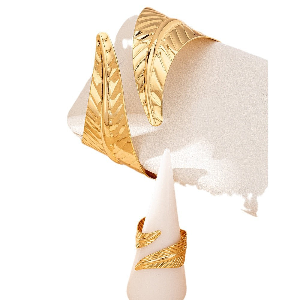 Gold feather-shaped open cuff bracelet on a white background