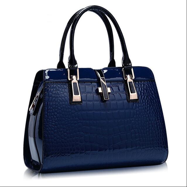 Blue crocodile pattern handbag with black handles on a white background