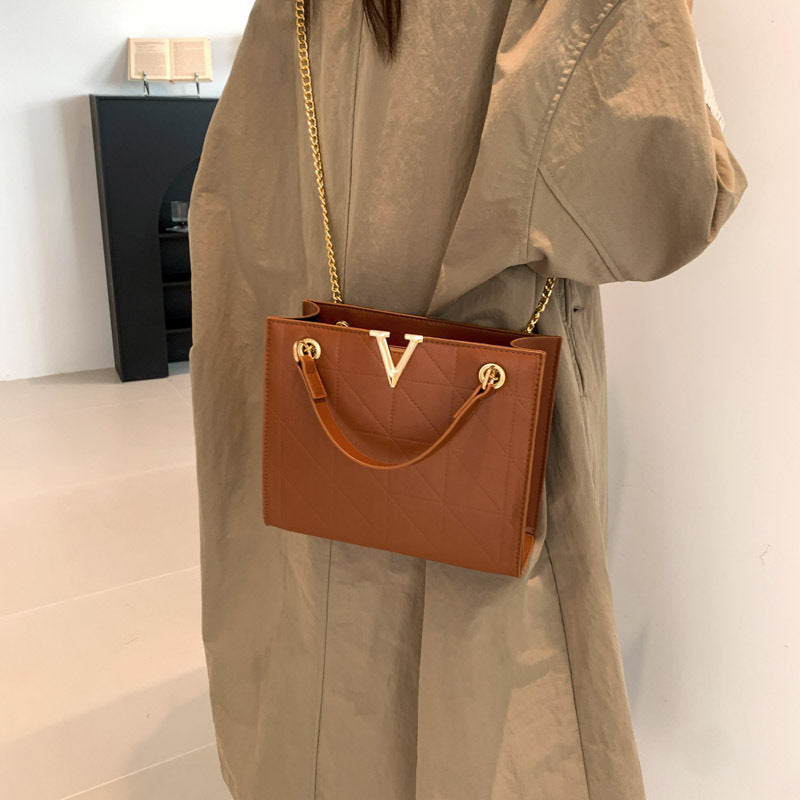 Person holding a brown women's leather crossbody bag with gold chain