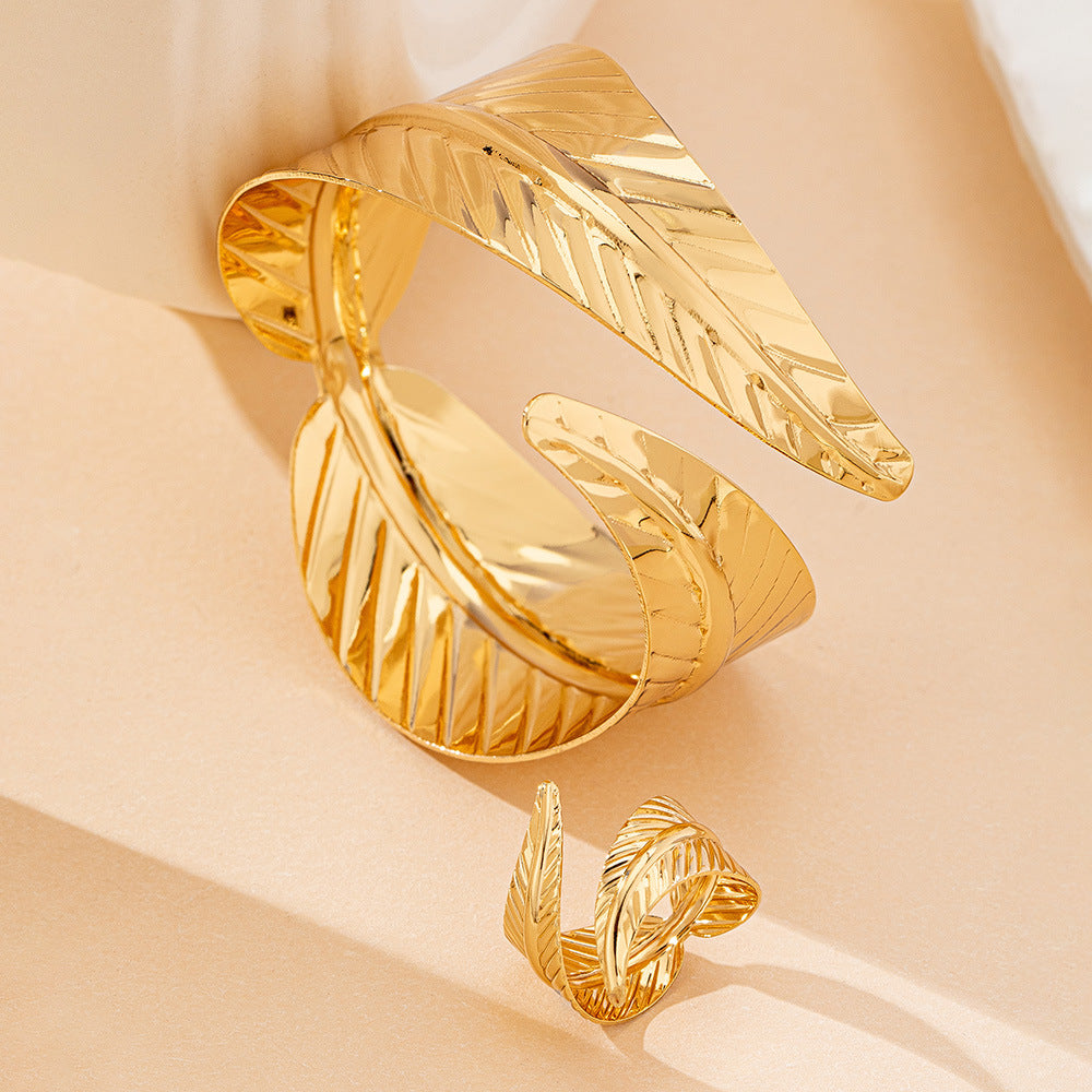 Gold leaf-shaped open cuff bracelet on a beige background