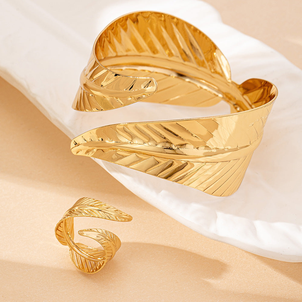 Gold leaf-shaped open cuff bracelet on a beige surface