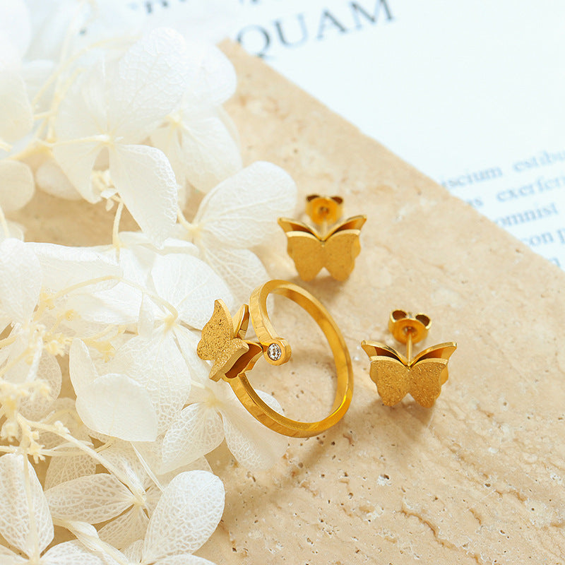 Gold butterfly earrings and ring on a textured surface with white flowers