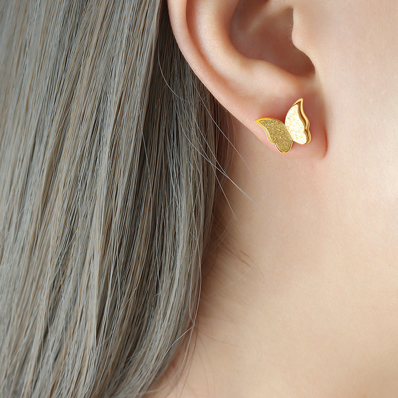 Gold butterfly earring worn by a person with gray hair.