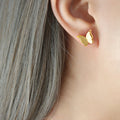 Gold butterfly earring worn by a person with gray hair.