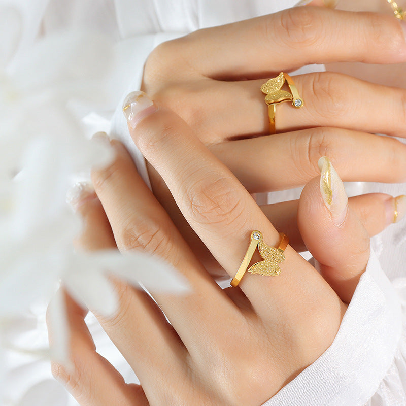 Close-up of hands wearing gold butterfly rings with a white background