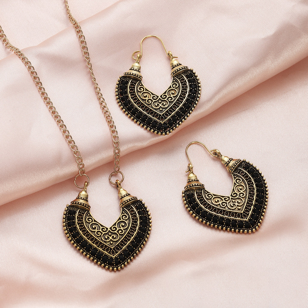 Ornate black and gold heart-shaped earrings and necklace on a pink fabric background