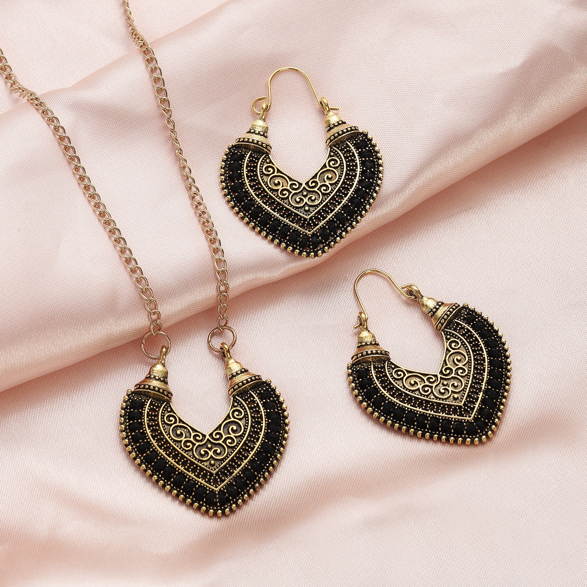 Ornate black and gold heart-shaped earrings and necklace on a pink fabric background