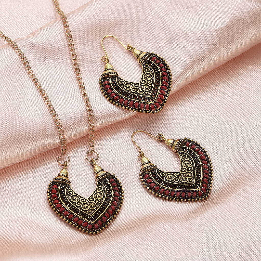 Pair of ornate heart-shaped earrings on a pink fabric background