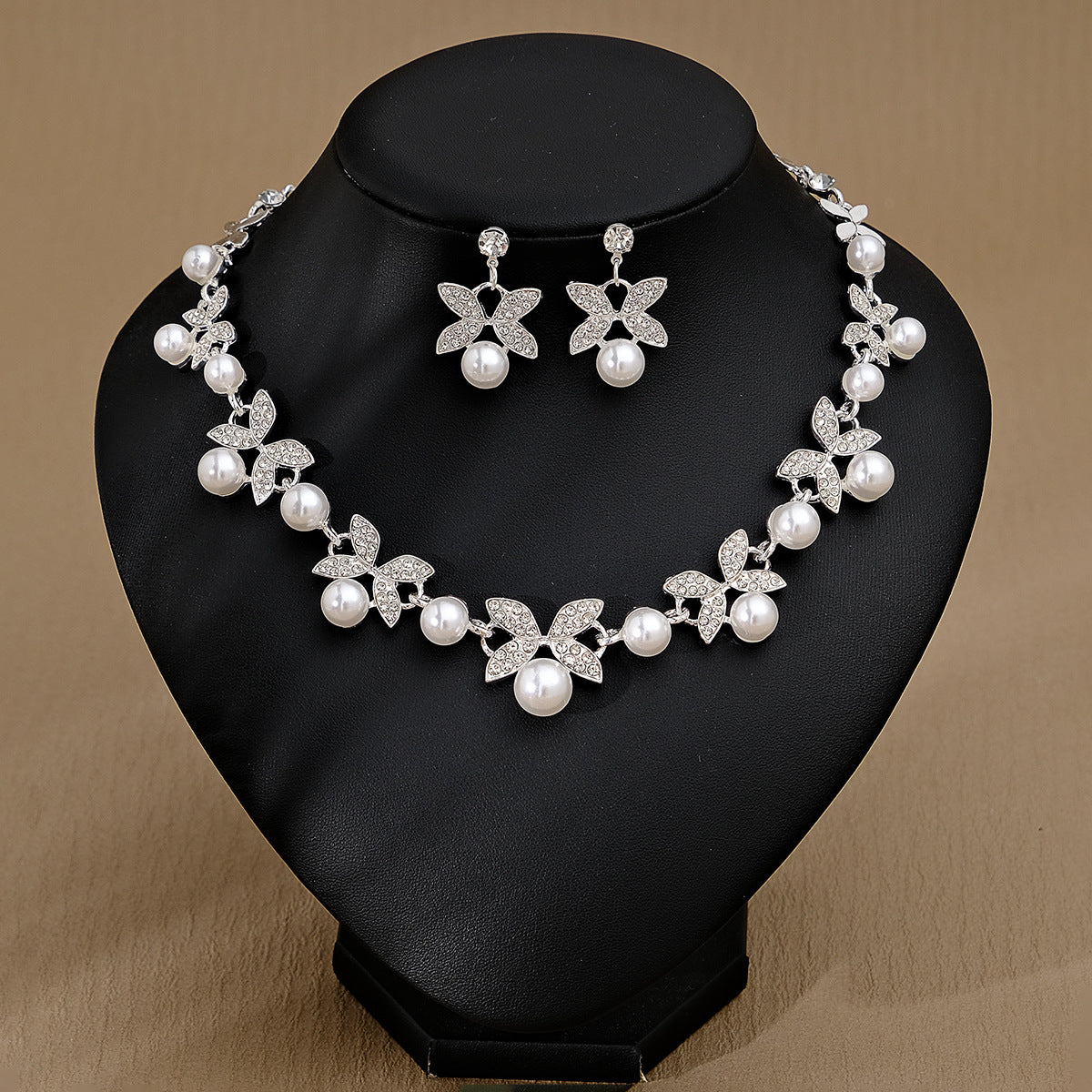 Pearl necklace and earrings set on a black stand with a brown background