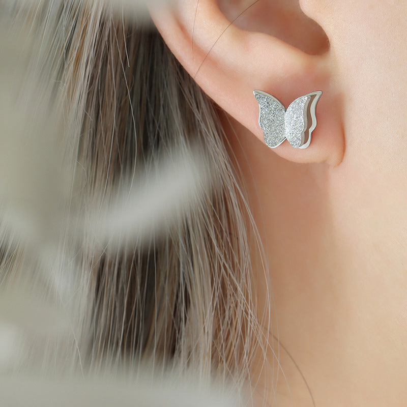 Silver butterfly earrings worn by a person with blurred background