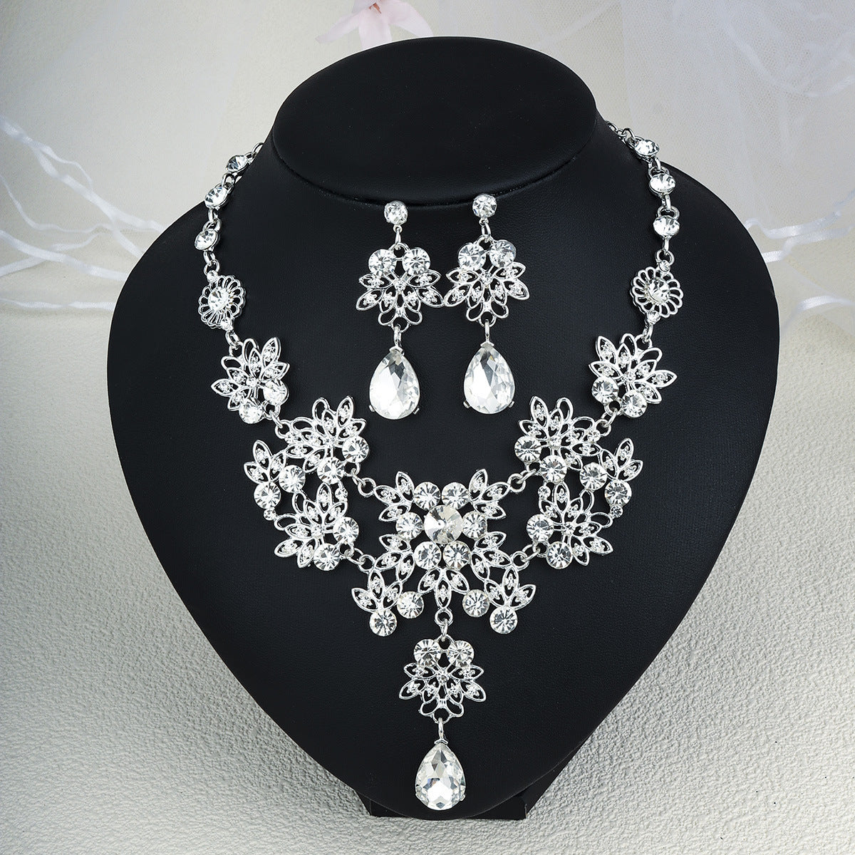 Silver pearl necklace and earrings set on a black heart-shaped stand.