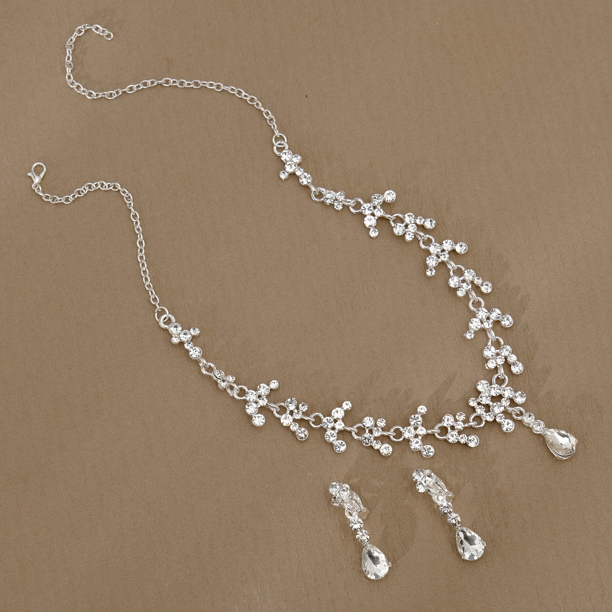 Silver pearl necklace and earrings set on a brown background